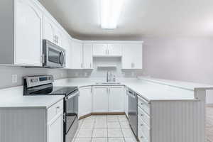 Kitchen with stainless steel appliances, a peninsula, white cabinetry, and light tile patterned floors