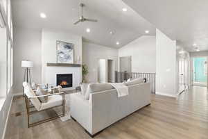 Living room with recessed lighting, light wood-type flooring, a glass covered fireplace, ceiling fan, and high vaulted ceiling