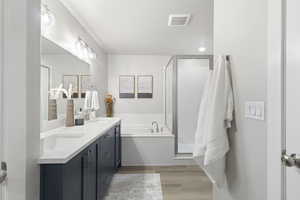 Full bath with double vanity, light wood-style floors, a stall shower, and a bath