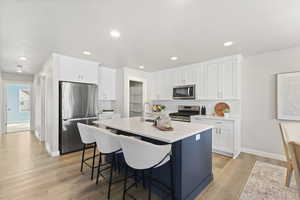 Kitchen featuring white cabinets, stainless steel appliances, a center island with sink, light wood finished floors, and recessed lighting