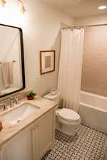 Full bathroom with vanity, shower / bath combo with shower curtain, and light tile patterned floors