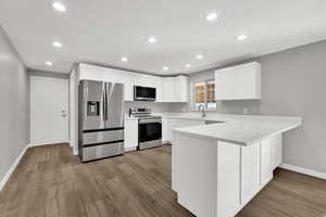 Kitchen with a peninsula, stainless steel appliances, white cabinetry, recessed lighting, and light wood-style floors