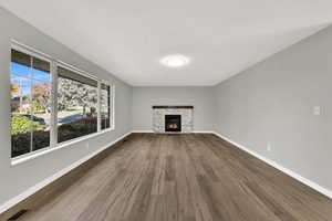 Unfurnished living room with a stone fireplace and dark wood-style flooring