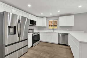 Kitchen featuring stainless steel appliances, a peninsula, white cabinets, light wood-style flooring, and recessed lighting