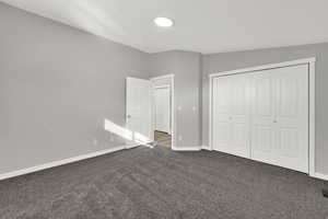 Unfurnished bedroom featuring dark colored carpet, a closet, and vaulted ceiling