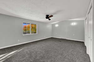 Empty room featuring dark colored carpet, a textured ceiling, vaulted ceiling, and a ceiling fan