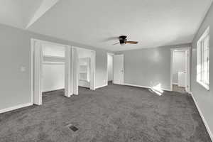 Unfurnished bedroom featuring multiple closets, dark colored carpet, a textured ceiling, and a ceiling fan