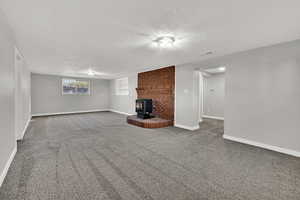 Unfurnished living room with carpet, a wood stove, and a textured ceiling