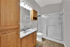 Full bathroom with light wood finished floors, vanity, a stall shower, and vaulted ceiling