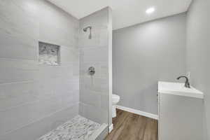 Bathroom with vanity, tiled shower, wood finished floors, and recessed lighting