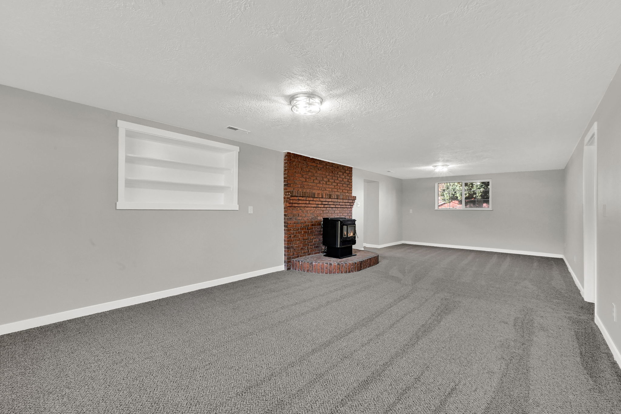 Unfurnished living room featuring built in shelves, carpet floors, a wood stove, and a textured ceiling