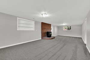 Unfurnished living room featuring built in shelves, carpet floors, a wood stove, and a textured ceiling