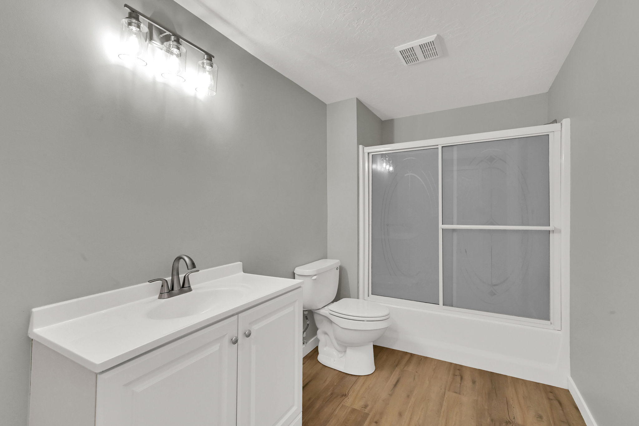 Bathroom featuring vanity, light wood-style flooring, shower / bath combination with glass door, and a textured ceiling
