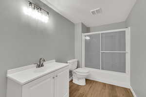 Bathroom featuring vanity, light wood-style flooring, shower / bath combination with glass door, and a textured ceiling