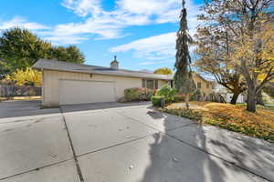 View of front of property featuring brick siding, concrete driveway, an attached garage, and a chimney