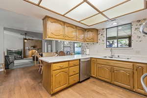Kitchen with light countertops, a peninsula, a fireplace, dishwasher, and light wood finished floors