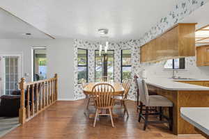 Dining room featuring wallpapered walls, dark wood-style flooring, and a textured ceiling