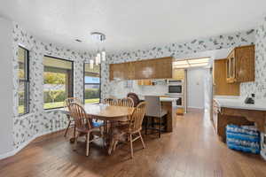 Dining area with wallpapered walls, light wood finished floors, and a textured ceiling