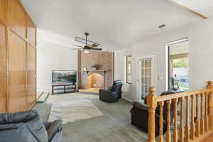 Carpeted living area with lofted ceiling, a brick fireplace, and a ceiling fan