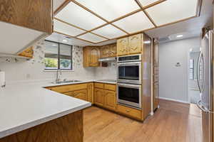 Kitchen featuring light countertops, light wood-type flooring, stainless steel appliances, brown cabinetry, and recessed lighting
