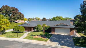 Ranch-style house featuring a front lawn, roof with shingles, concrete driveway, and brick siding