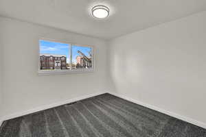 Spare room featuring dark carpet and a textured ceiling