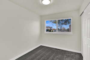 Unfurnished bedroom with dark carpet, a closet, and a textured ceiling