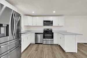 Kitchen featuring stainless steel appliances, a peninsula, white cabinetry, light wood finished floors, and recessed lighting