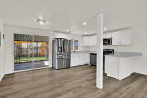 Kitchen featuring appliances with stainless steel finishes, white cabinets, light countertops, light wood-type flooring, and a peninsula