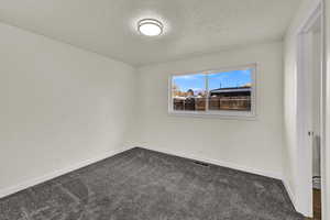 Empty room with dark colored carpet and a textured ceiling