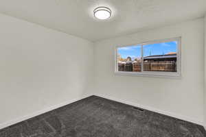 Empty room featuring dark carpet and a textured ceiling