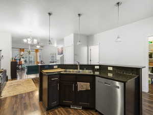 Kitchen featuring stainless steel dishwasher, hanging light fixtures, a kitchen island with sink, open floor plan, and dark wood finished floors