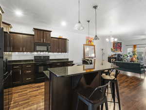 Kitchen featuring dark brown cabinets, black appliances, a kitchen breakfast bar, a chandelier, and a kitchen island with sink