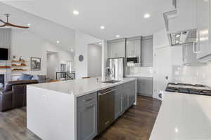 Kitchen with gray cabinets, open floor plan, lofted ceiling, backsplash, and appliances with stainless steel finishes