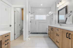 Full bath with double vanity, light tile patterned flooring, and a shower stall