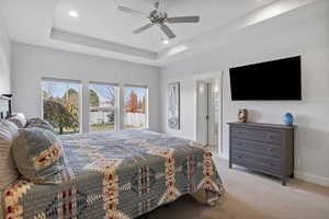 Bedroom featuring carpet flooring, a raised ceiling, ensuite bathroom, ceiling fan, and recessed lighting