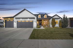 Modern farmhouse with board and batten siding, a garage, driveway, a front lawn, and a standing seam roof