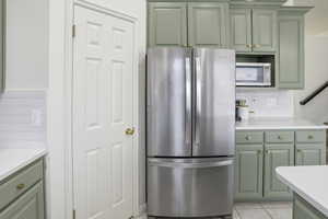 Kitchen with green cabinets, tasteful backsplash, stainless steel appliances, and light tile patterned floors