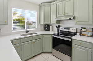 Kitchen featuring stainless steel electric range, green cabinets, backsplash, under cabinet range hood, and light tile patterned floors