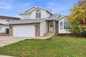 View of front of property with a shingled roof, driveway, a front lawn, a garage, and brick siding