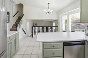 Kitchen with green cabinets, appliances with stainless steel finishes, light tile patterned floors, pendant lighting, and a peninsula
