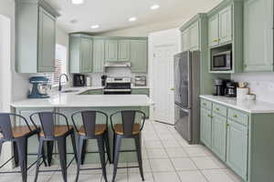 Kitchen with green cabinets, decorative backsplash, a breakfast bar area, appliances with stainless steel finishes, and a peninsula