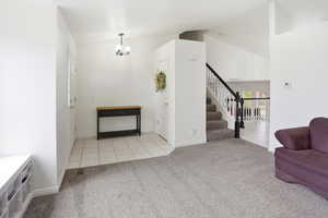 Foyer entrance featuring light tile patterned floors, light carpet, vaulted ceiling, stairway, and a chandelier