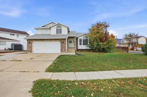 Traditional home featuring a front lawn, driveway, an attached garage, brick siding, and roof with shingles