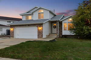 View of front of house featuring concrete driveway, a lawn, an attached garage, a shingled roof, and brick siding