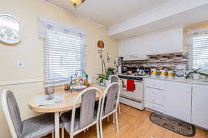 Kitchen with white cabinets, white electric stove, light countertops, decorative backsplash, and light wood-style floors