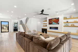 Living area with a large fireplace, light wood-type flooring, stairway, recessed lighting, and ceiling fan