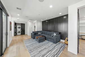 Living room with stacked washer / dryer, light wood-style flooring, recessed lighting, wood walls, and an accent wall
