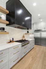 Kitchen with open shelves, custom exhaust hood, recessed lighting, appliances with stainless steel finishes, and decorative backsplash