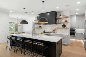 Kitchen with open shelves, light stone countertops, decorative light fixtures, tasteful backsplash, and dark cabinetry